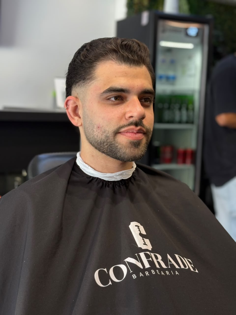 Cliente da Confrade com corte finalizado usando a capa da barbearia
